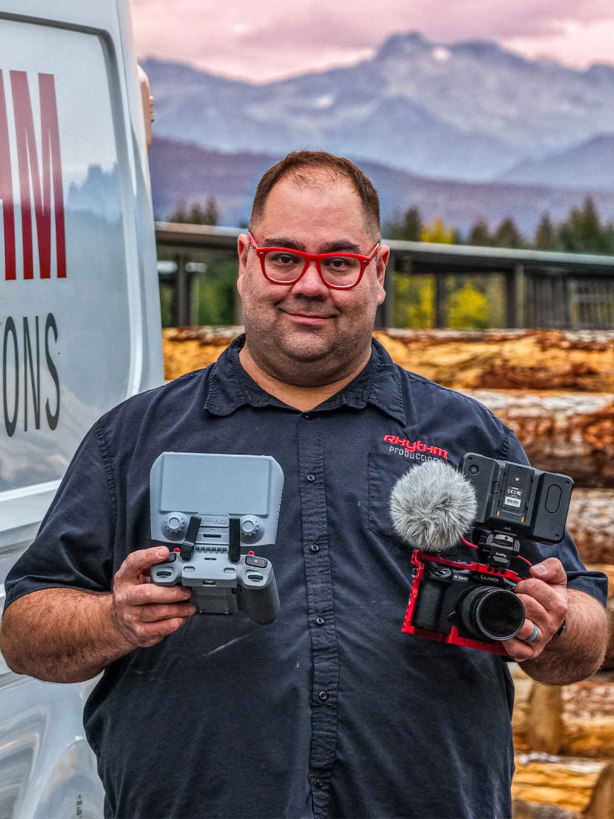 Mike Babott of Rhythm Productions holding a camera rig and a drone controller beside his work van