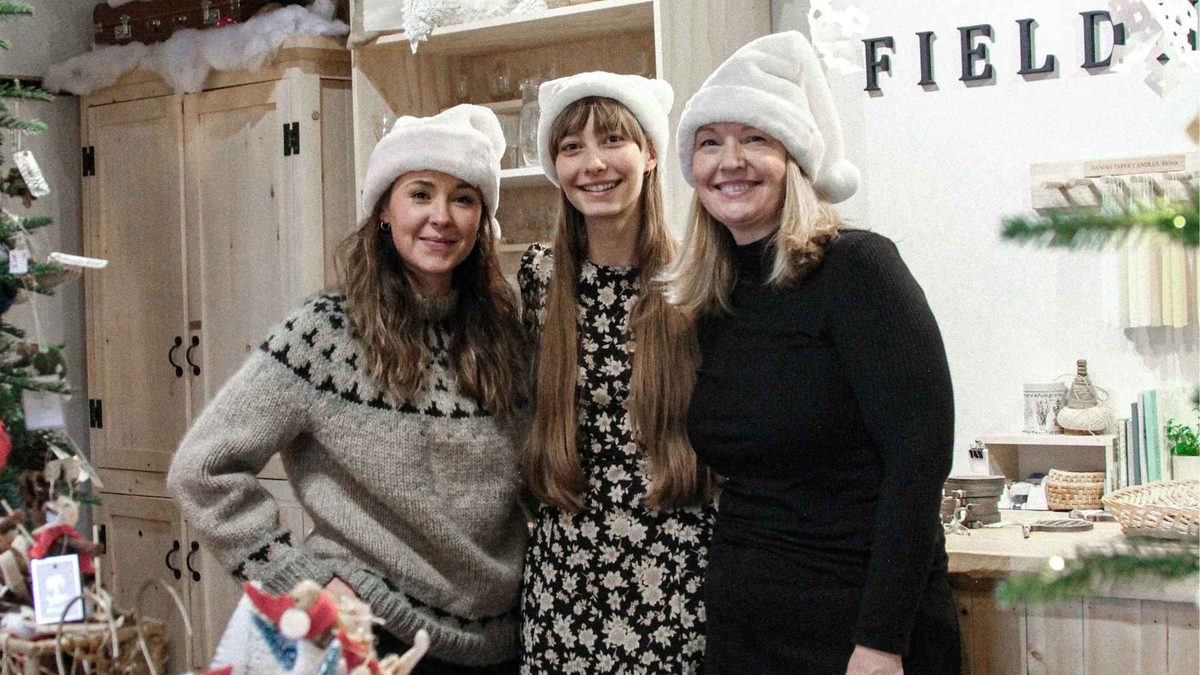 Three shop owners in Santa hats at a decorated Armstrong storefront