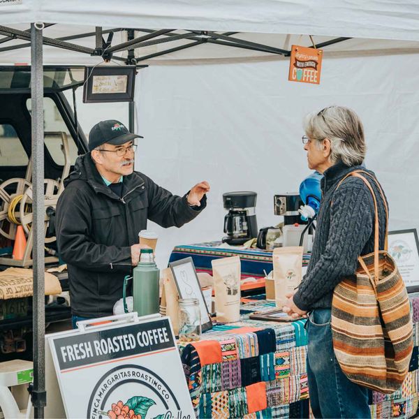 A coffee roaster serving a customer at his market stall