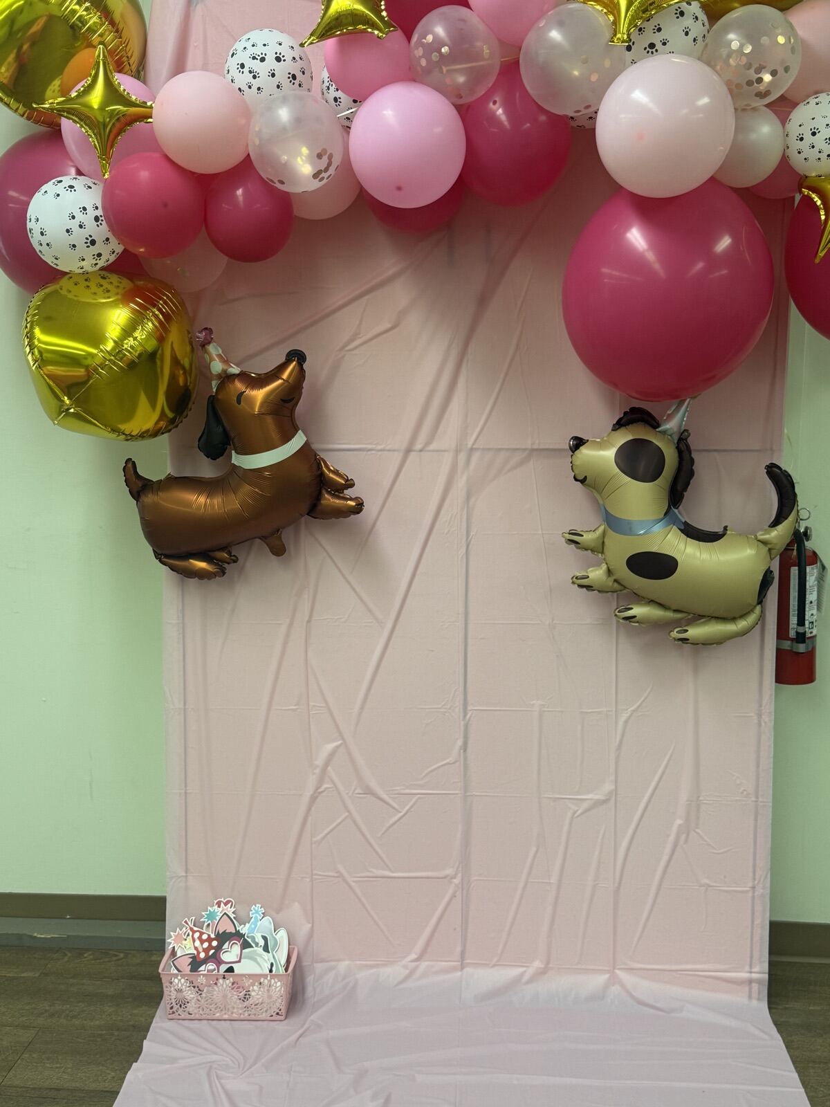 A pink balloon arch photo backdrop with two puppy balloons