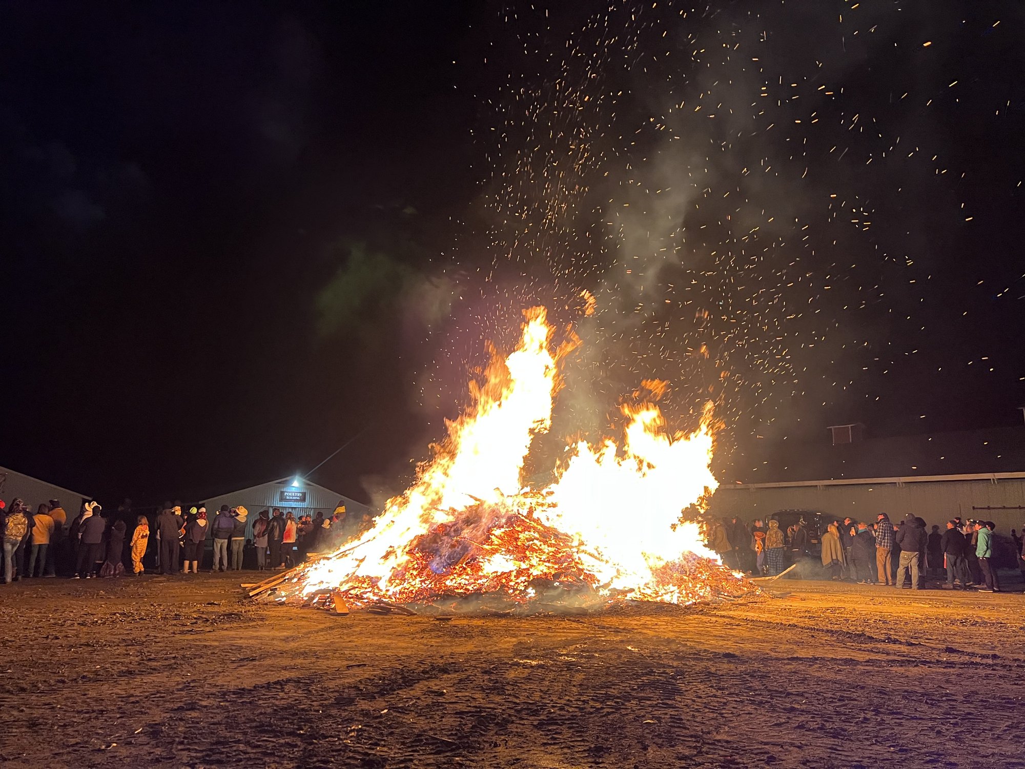 A Halloween bonfire at the Armstrong Spallumcheen Fair Grounds, with people gathered around the fire.