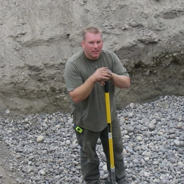 Darren Wallace holding a shovel beside a septic tank