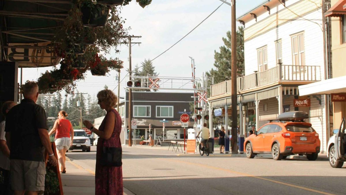 People walking past storefronts and hanging flower baskets on a summer evening in downtown Armstrong, BC