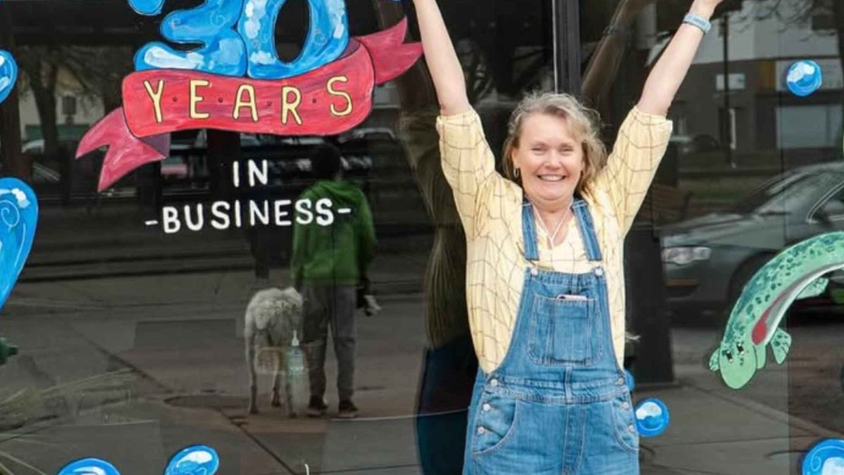 A business owner celebrating 30 years in front of her painted storefront window